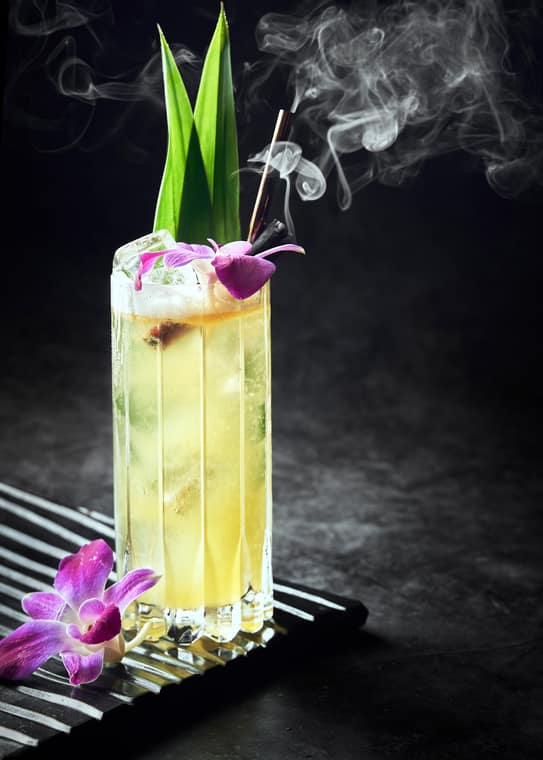 Tall smoky cocktail with green leaves and an orchid